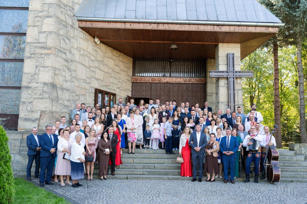 Zdjęcie grupowe wszystkich gości przed kamiennym kościołem