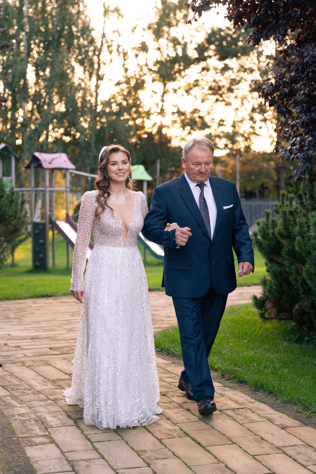 Ojciec prowadzi pannę młodą ogrodową alejką na ceremonię