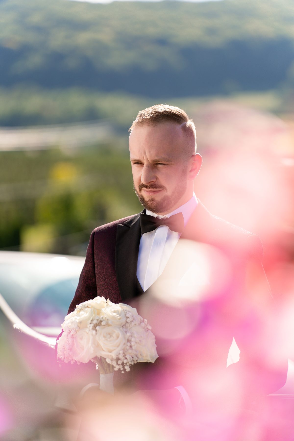 Pan młody z bukietem, w tle beskidzkie wzgórza za rozmytymi kwiatami